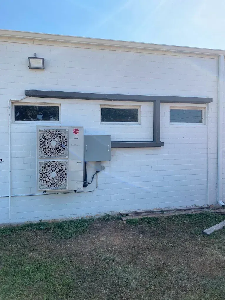White building exterior with windows, mounted HVAC units, and a small grassy yard.