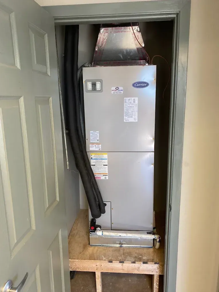 HVAC unit installed in a closet doorway with exposed ductwork above and a wooden platform below
