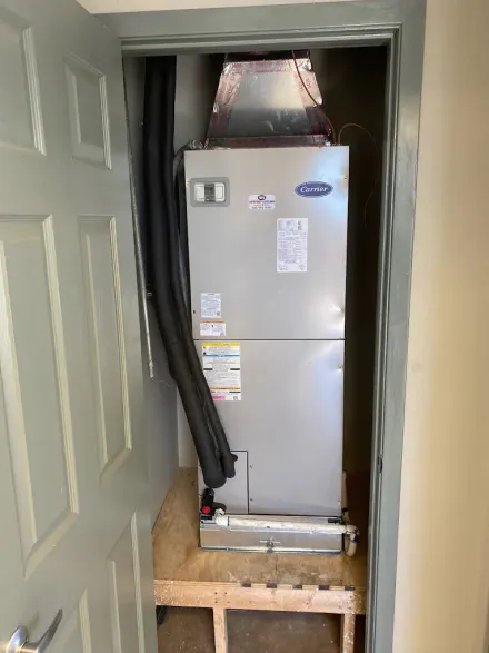 Tall HVAC unit installed in a narrow doorway, with exposed ducting and unfinished flooring nearby