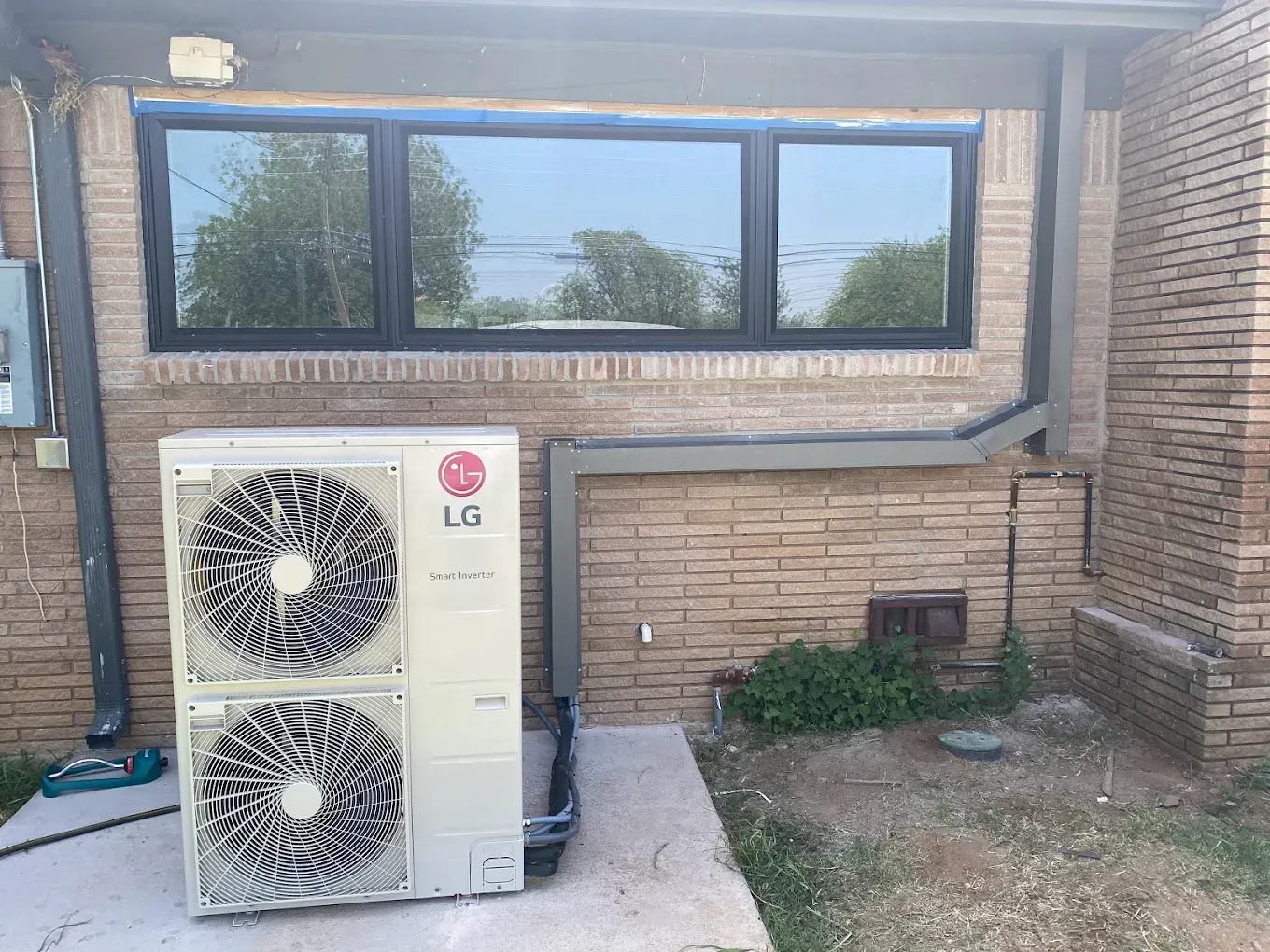 LG outdoor AC unit against a brick wall beside windows in a courtyard