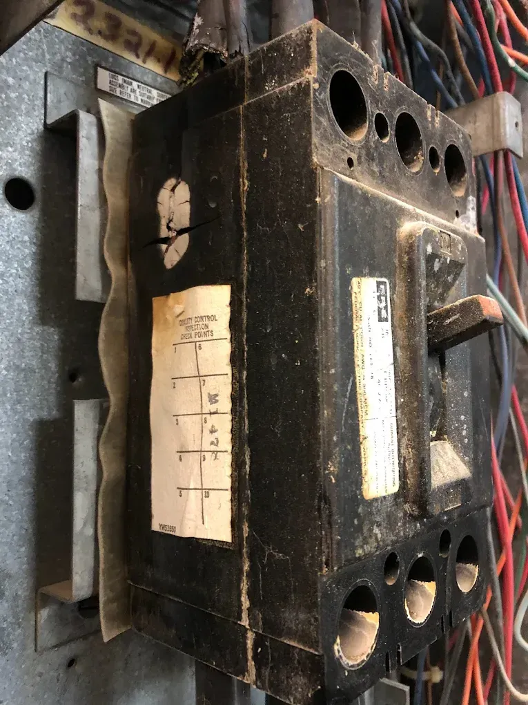 Close-up of a black metal electrical device with wires and labels mounted on a workbench