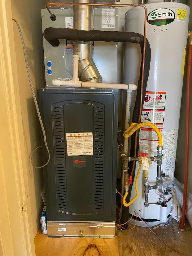 Water heater and furnace in a narrow utility closet with exposed pipes and hoses.
