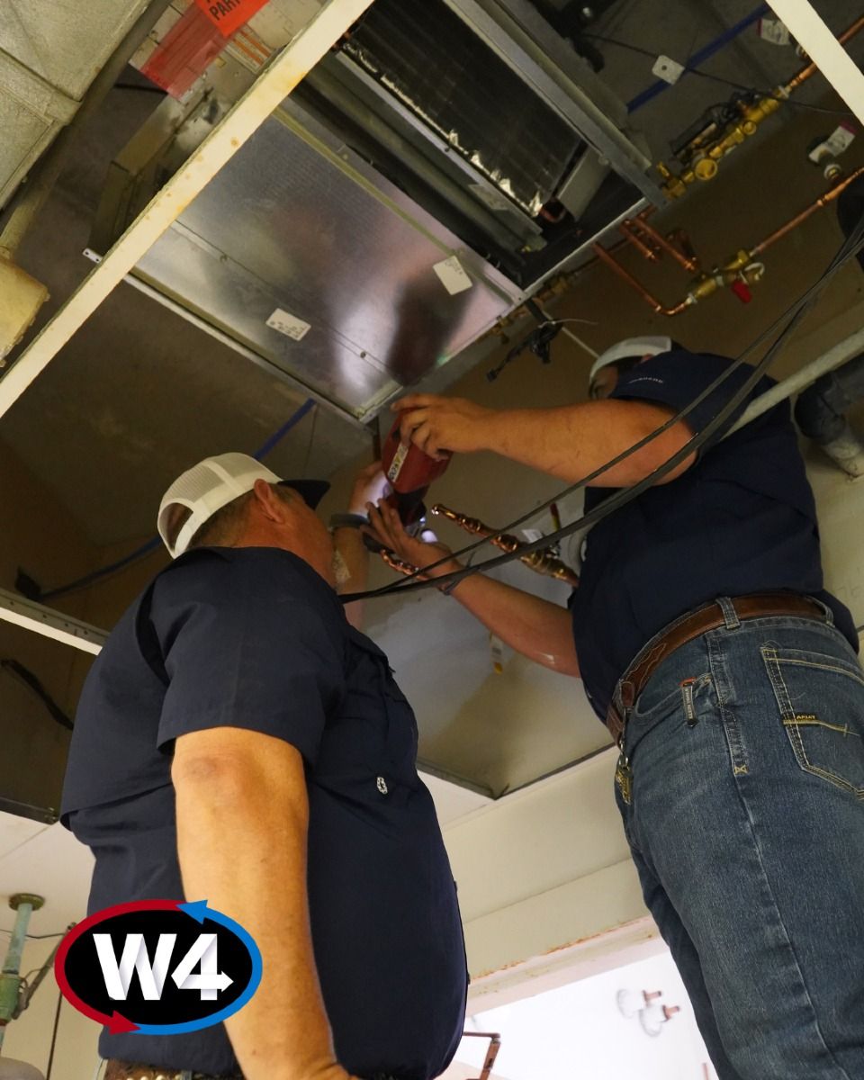 Two workers inspecting and repairing an overhead ceiling panel with tools, one wearing a hard hat.
