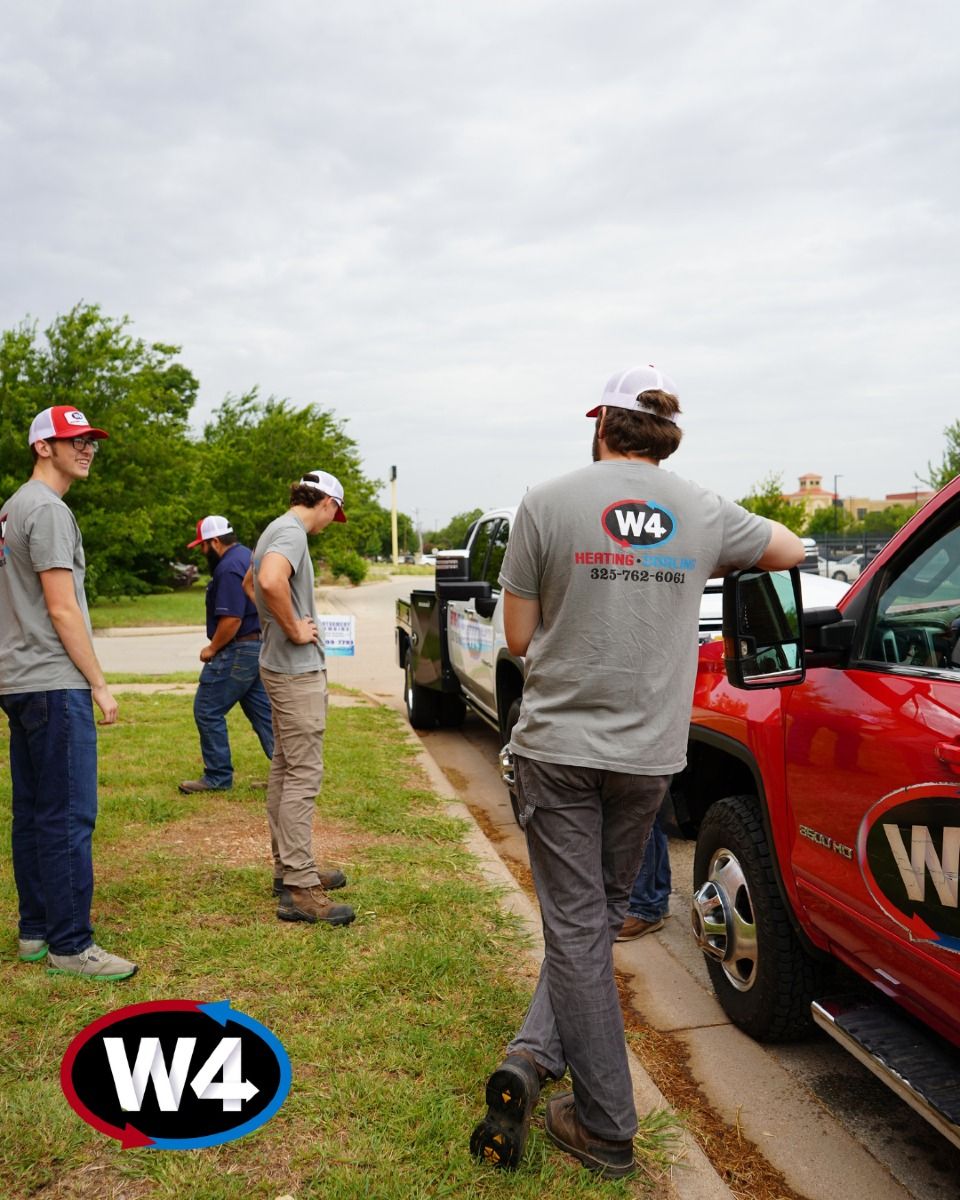 W4 workers standing by a red truck on a grassy roadside, one loading gear near the curb