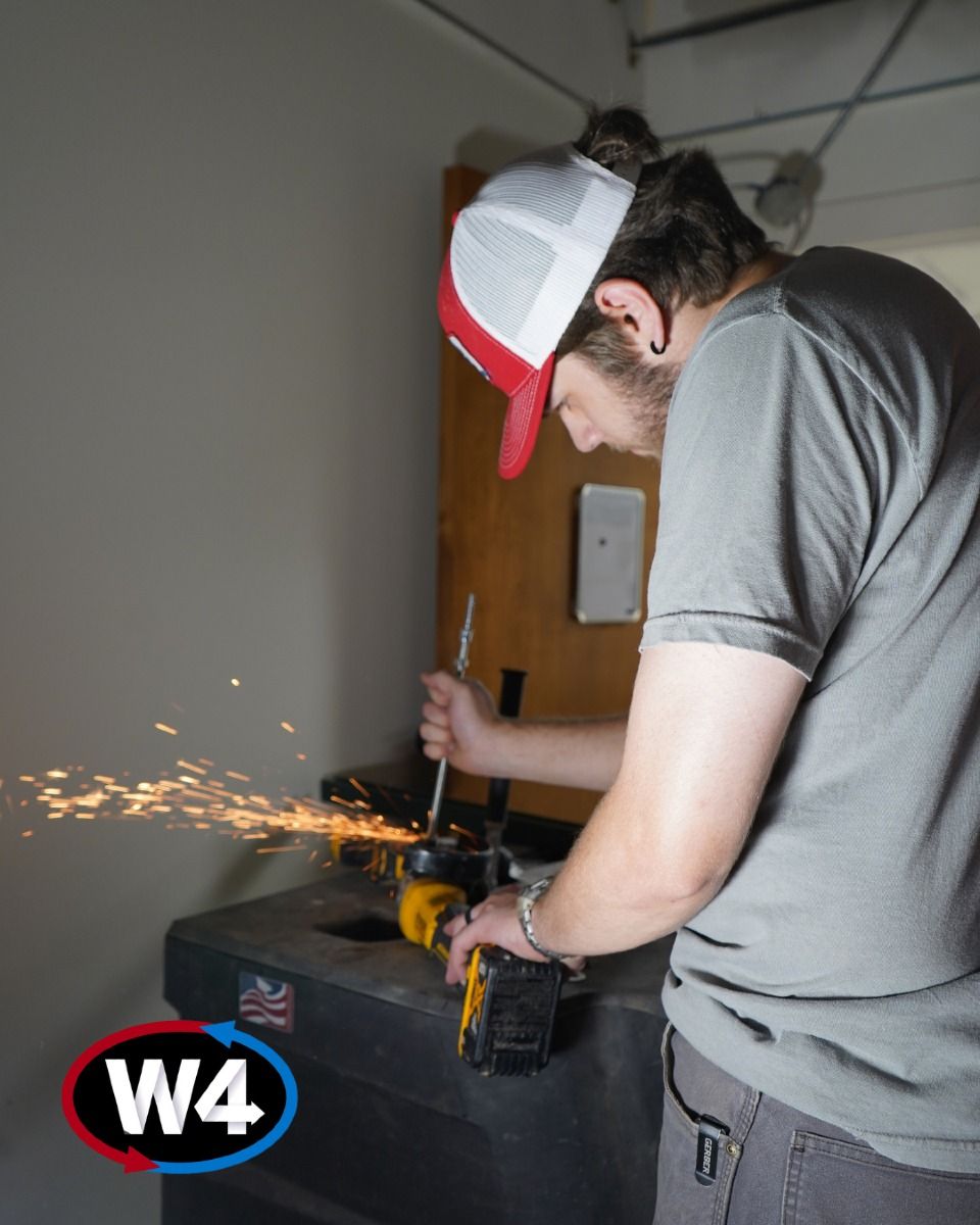 Person using a power tool sparks in a workshop, wearing a red-and-white cap and gray shirt.