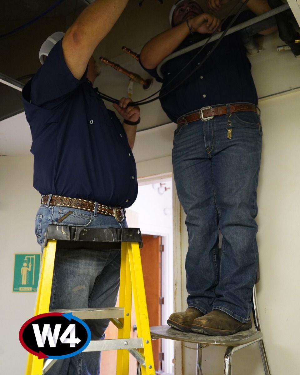 Two workers on ladders fixing ceiling wiring in a room