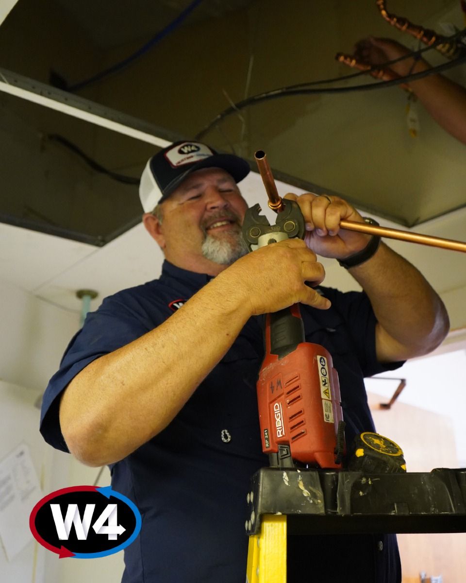 Man using a red drill overhead on a ladder, wearing a cap in a workshop or garage