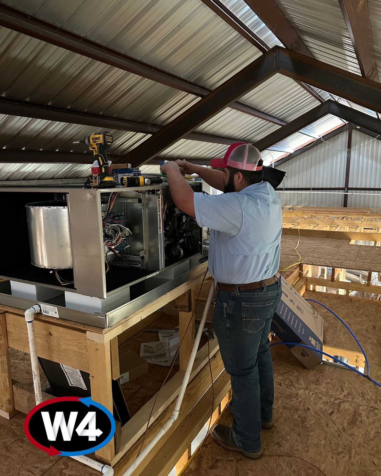 Worker in a pink hard hat adjusting a large machine inside a barn-like workshop.
