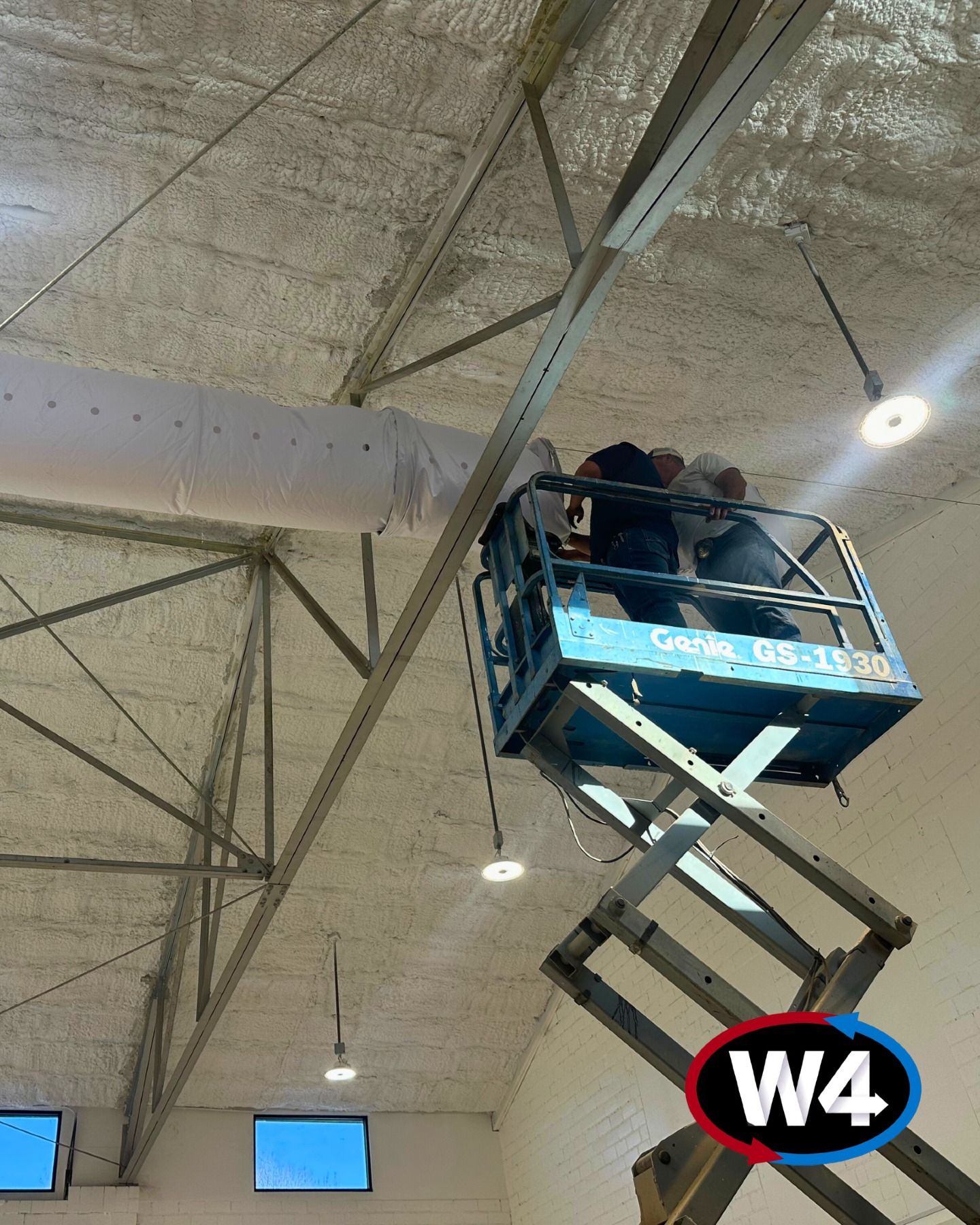 Workers in a blue scissor lift inspecting a ceiling inside a warehouse, labeled W4.