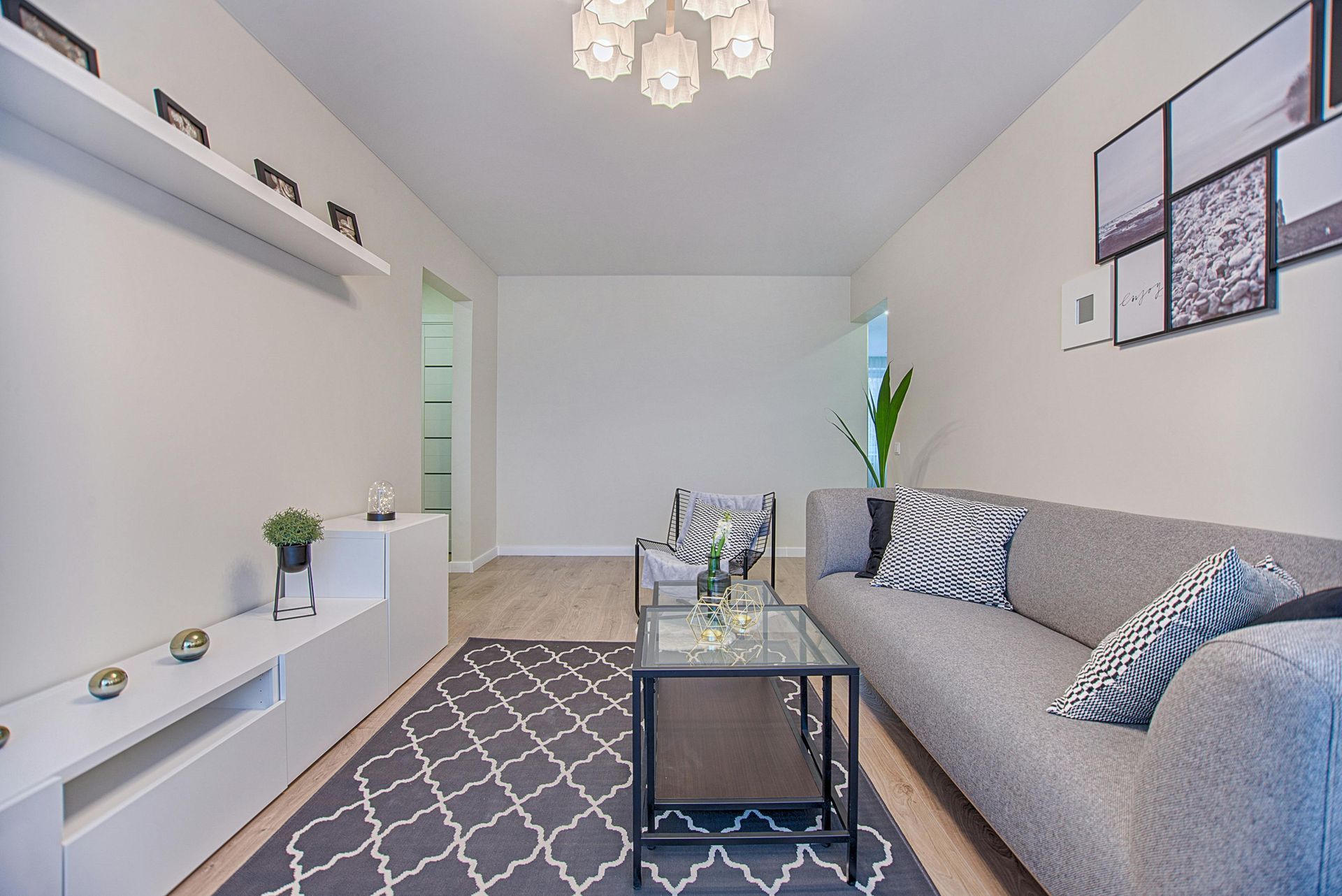 Modern living room with gray sofa, patterned rug, glass coffee table, and white wall shelving