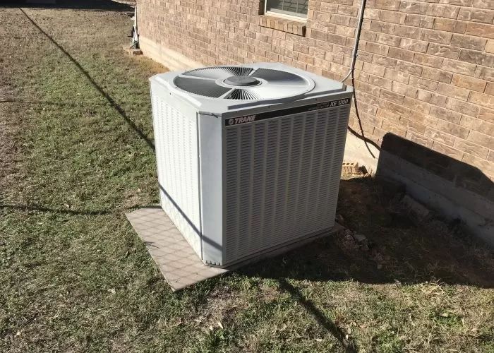 Outdoor air conditioning unit beside a brick house on a grassy lawn.