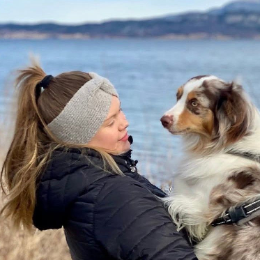Woman in winter headband holding a brown-and-white dog by the water