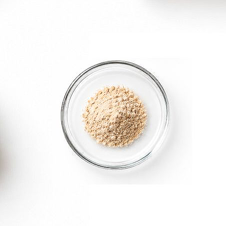 A small glass bowl filled with beige powder on a white background