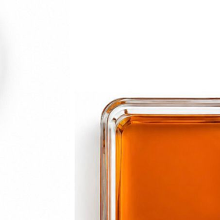 Close-up of a square glass dish filled with orange liquid on a white background