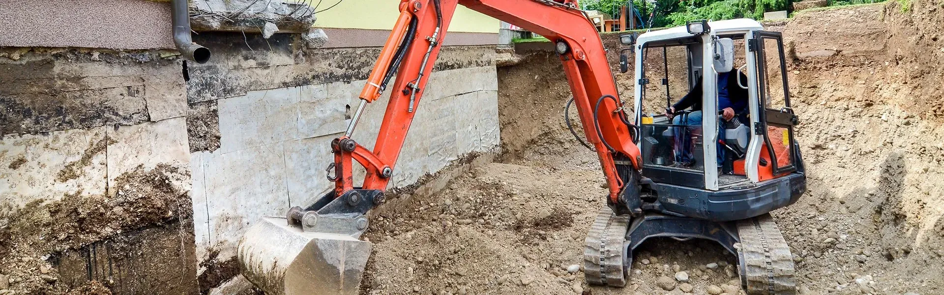 A man is driving an excavator in a dirt field.