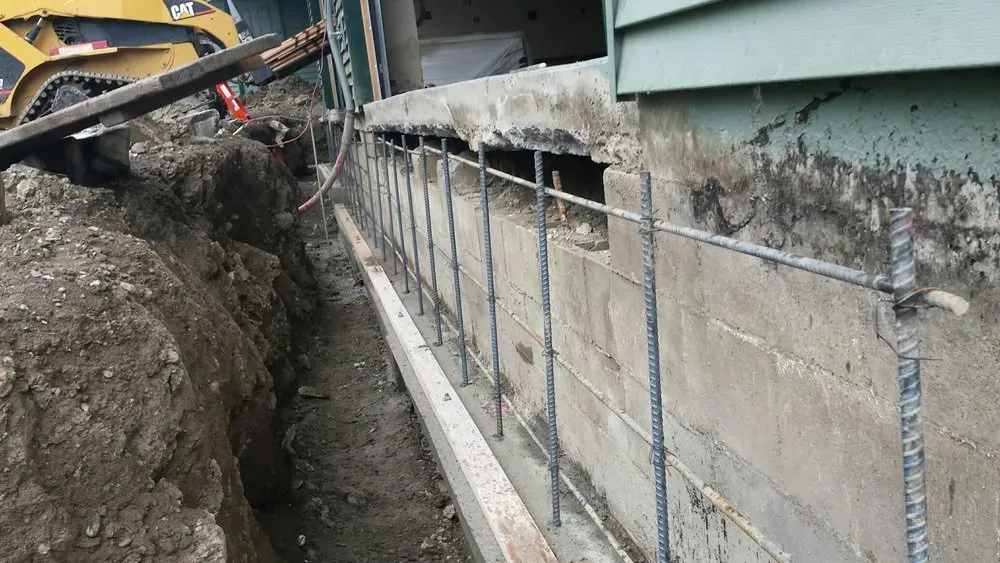 A bulldozer is digging a hole in the ground next to a brick wall.