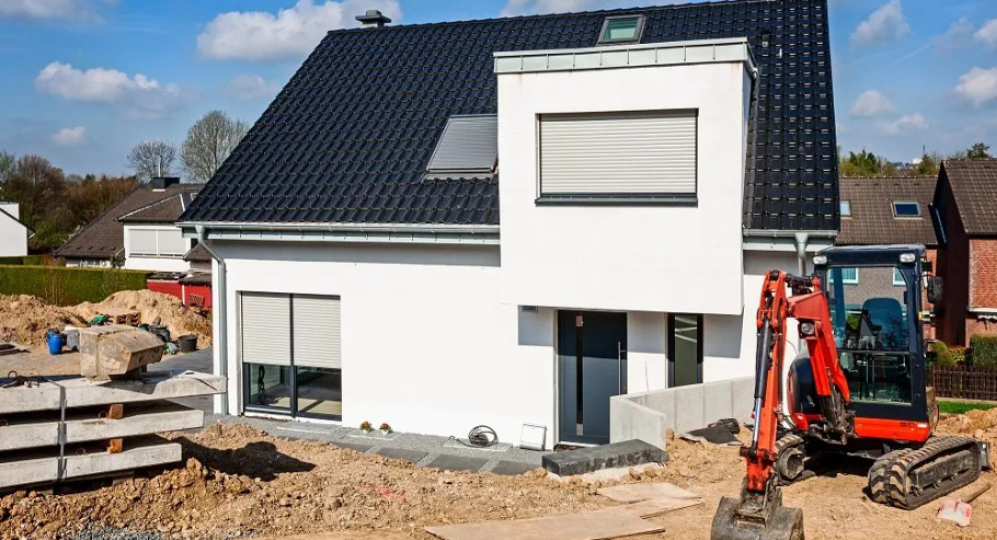 A small excavator is parked in front of a house under construction.