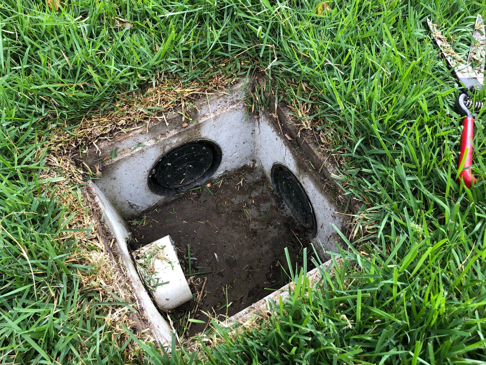A hole in the ground in the grass next to a pair of scissors.