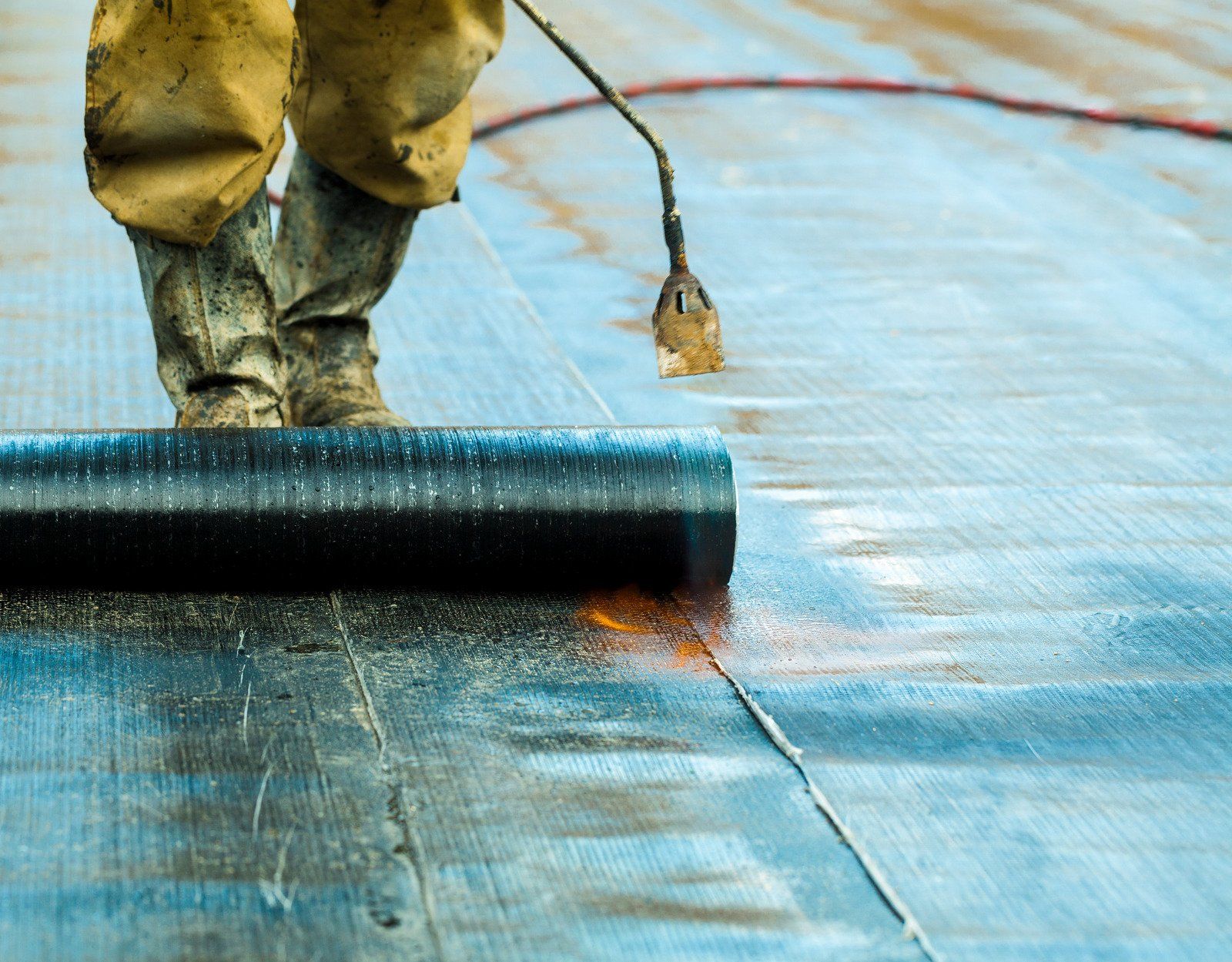 A person is rolling a roll of waterproofing on a roof.