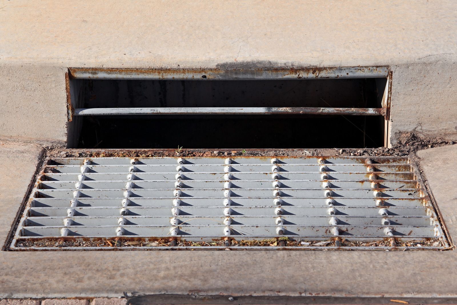 Ground-level air vent and metal grate set into concrete pavement