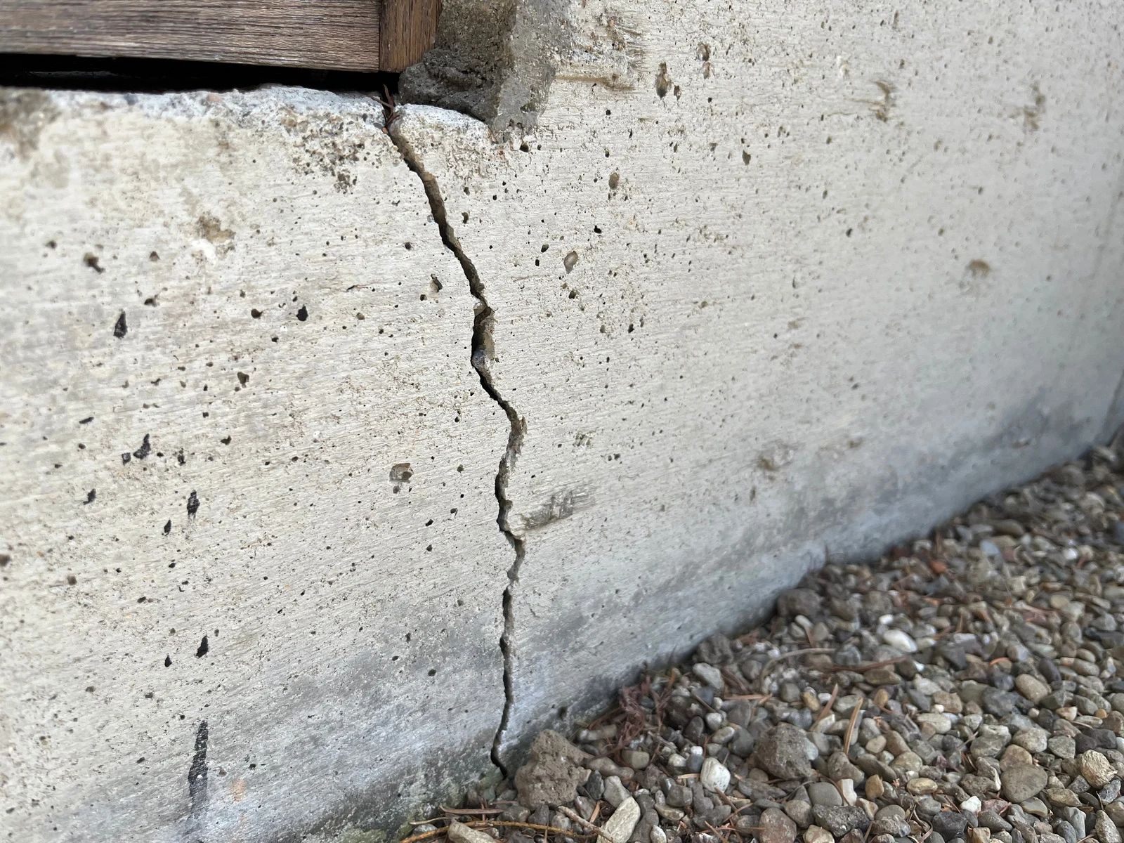 Cracked concrete foundation wall with a vertical fissure near gravel ground.