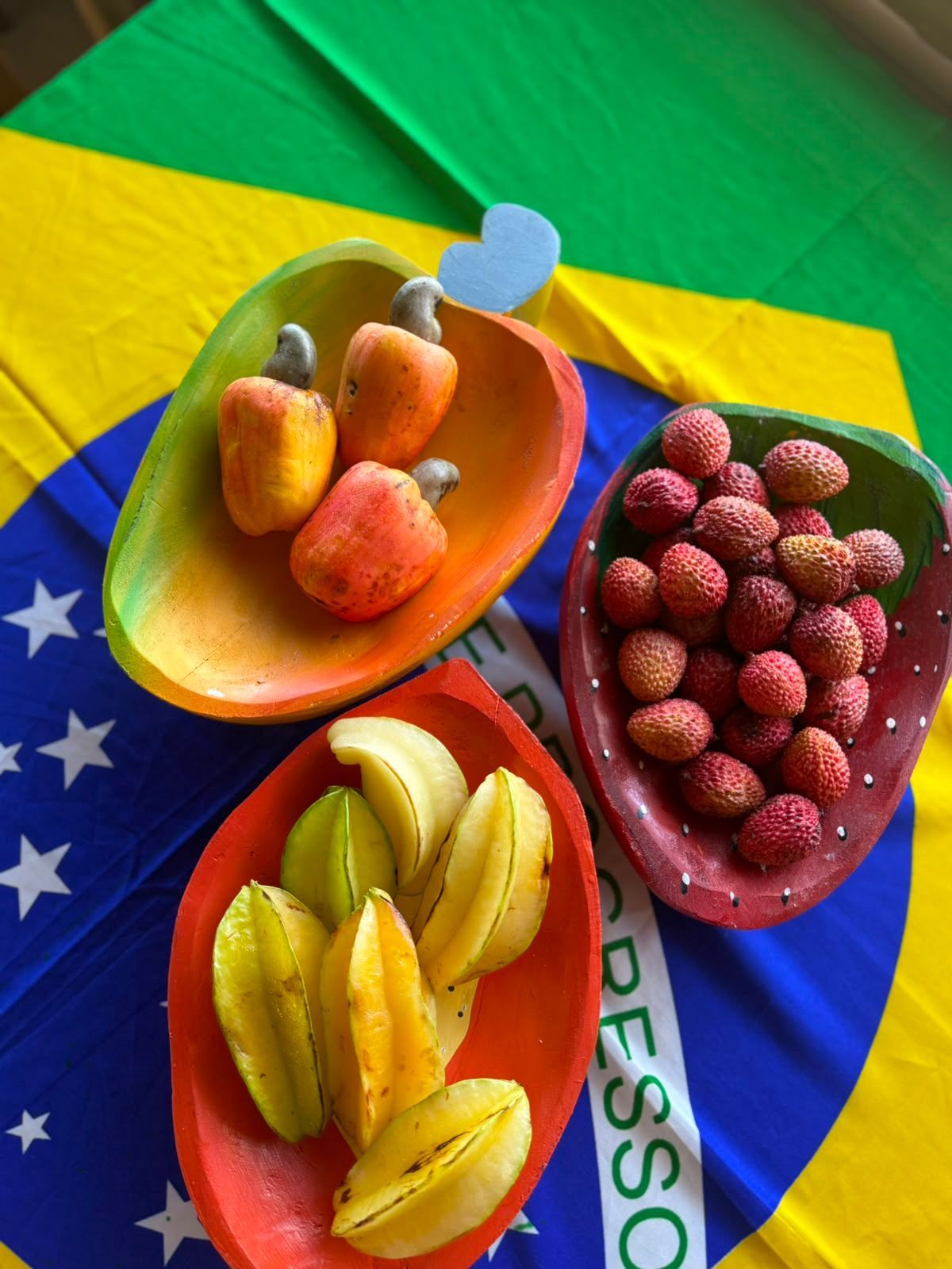 Três tigelas de frutas coloridas sobre um pano brilhante com estampa de bandeira.