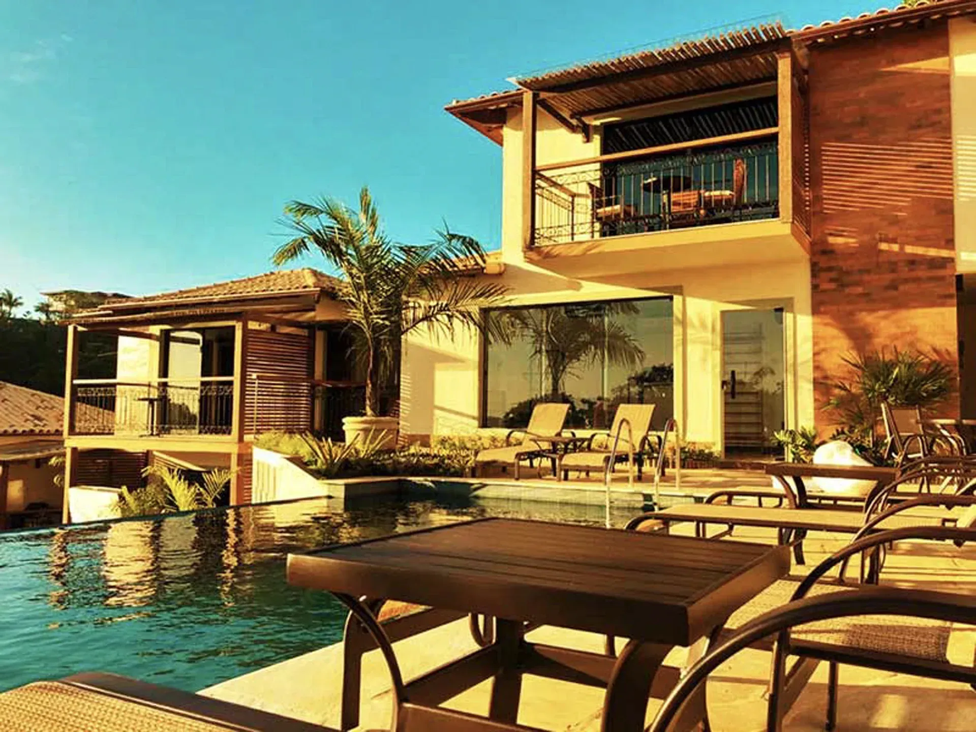 Pátio de resort de luxo com piscina, espreguiçadeiras e moderna villa de madeira sob a luz solar.