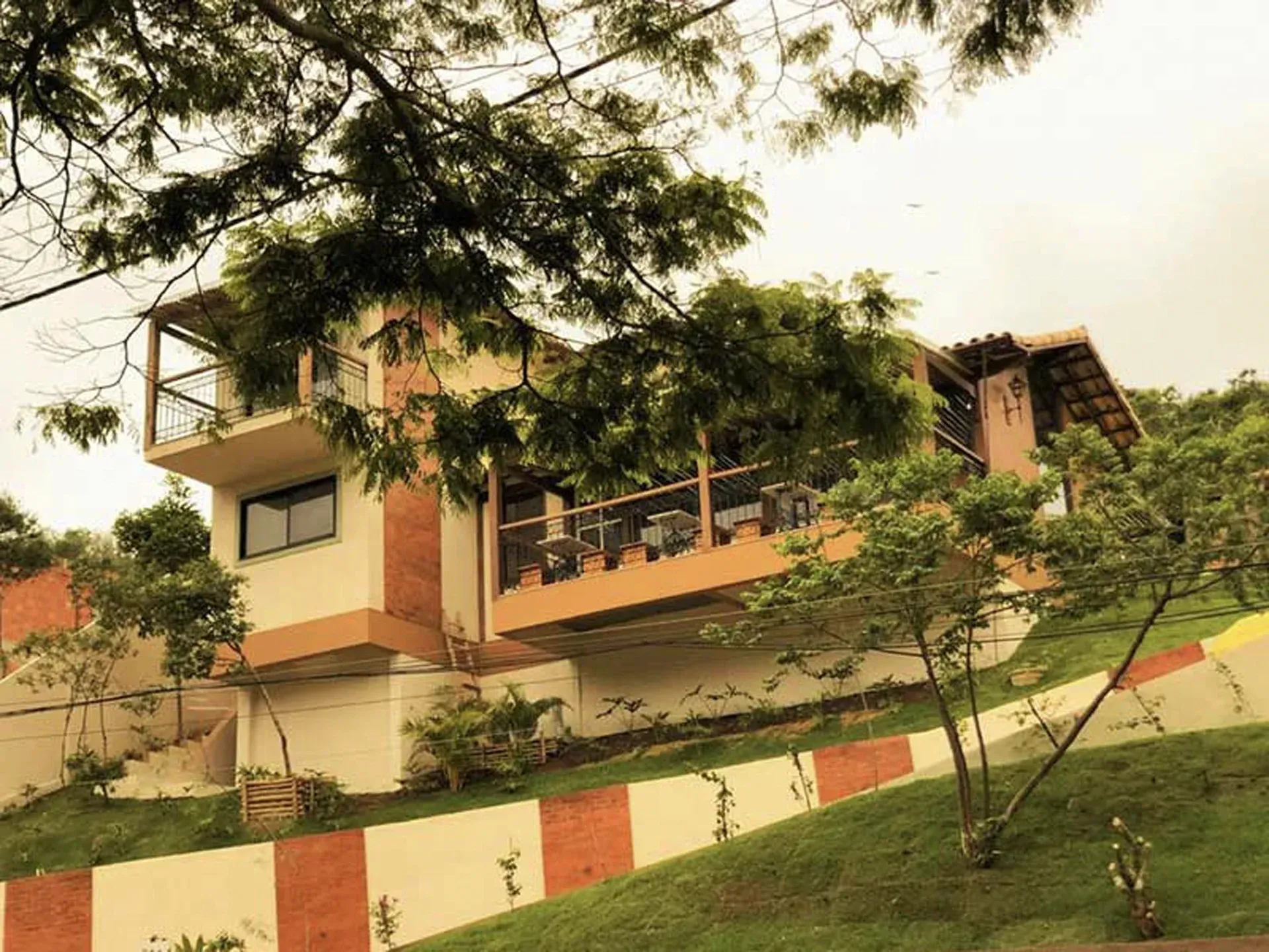 Casa moderna em uma encosta com árvores e um muro de contenção vermelho e branco.