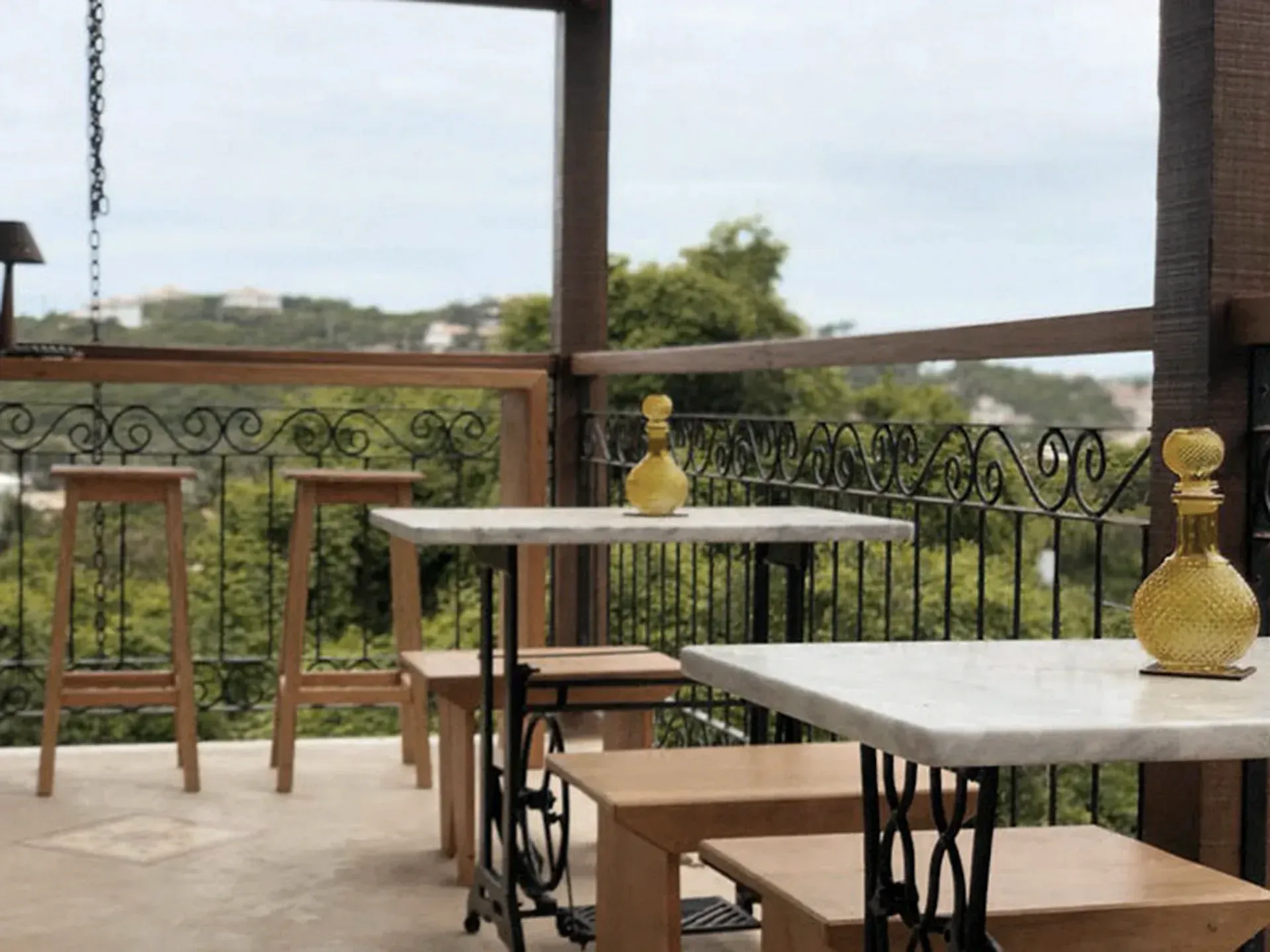 Mesas de café ao ar livre com mesas brancas, bancos de madeira e vasos decorativos amarelos em um terraço coberto.