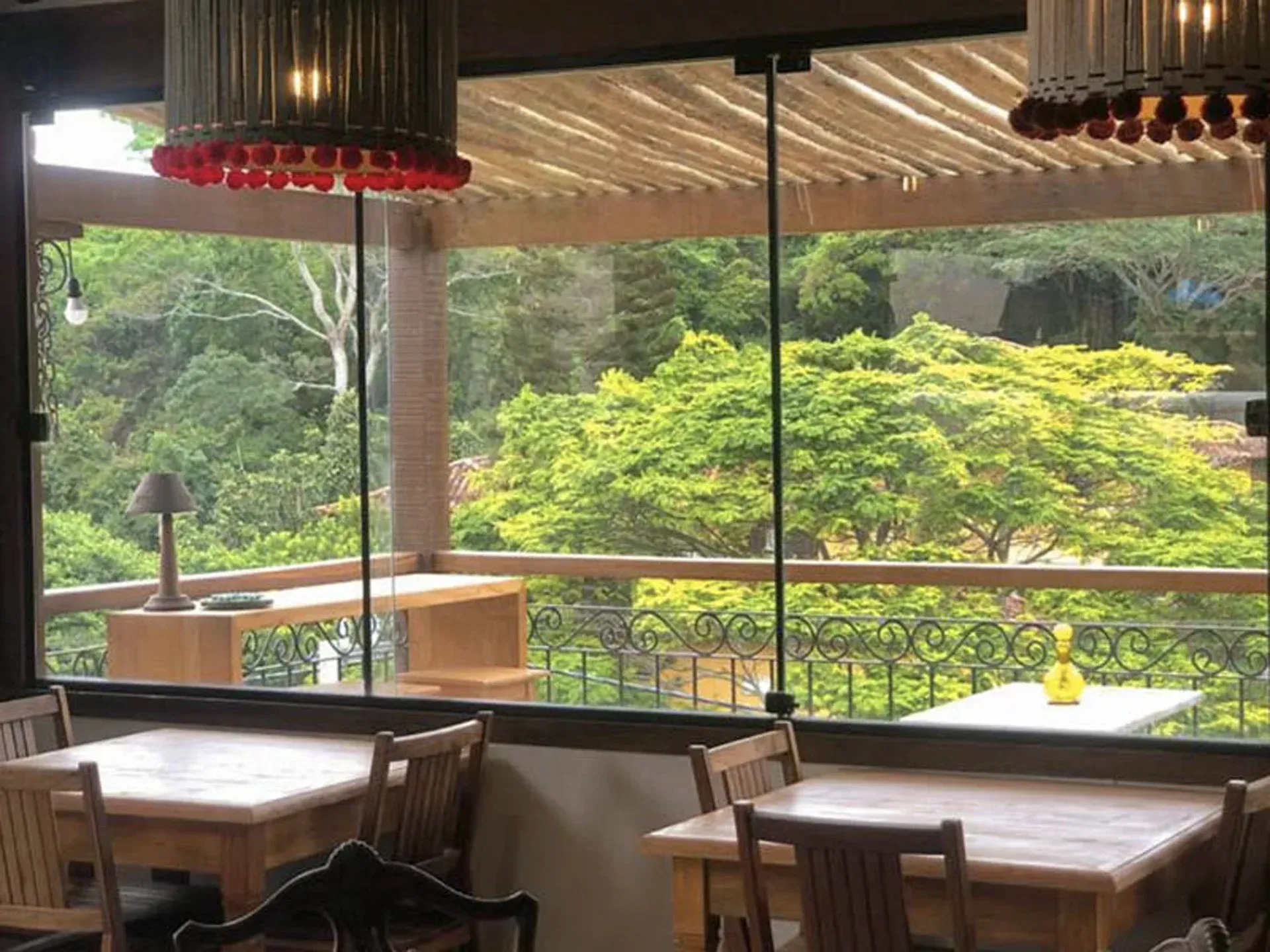 Restaurante vazio com mesas de madeira com vista para árvores verdejantes através de grandes janelas.