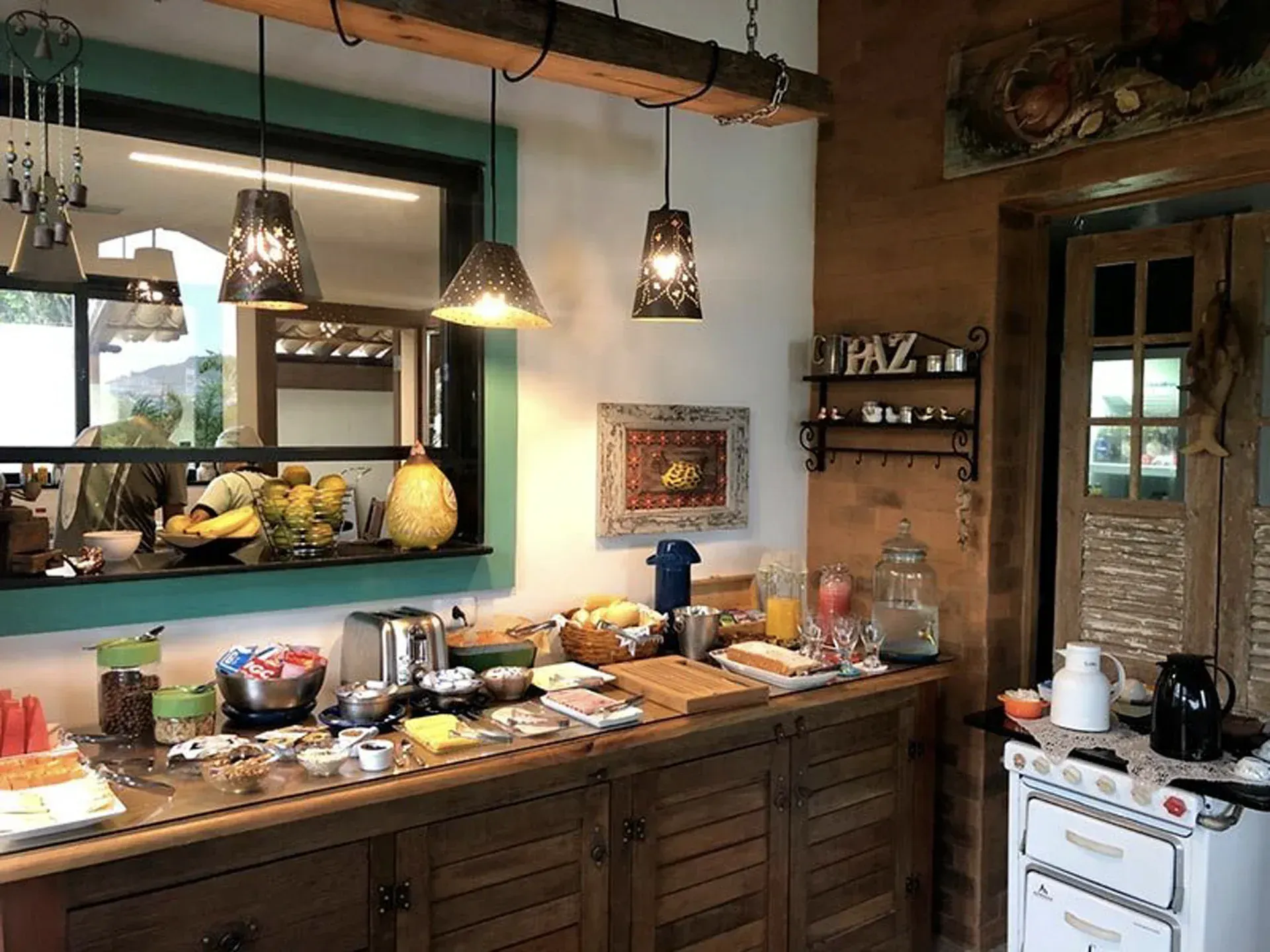 Cozinha aconchegante com bancada de madeira, luminárias pendentes, vitrine para alimentos e fogão branco.