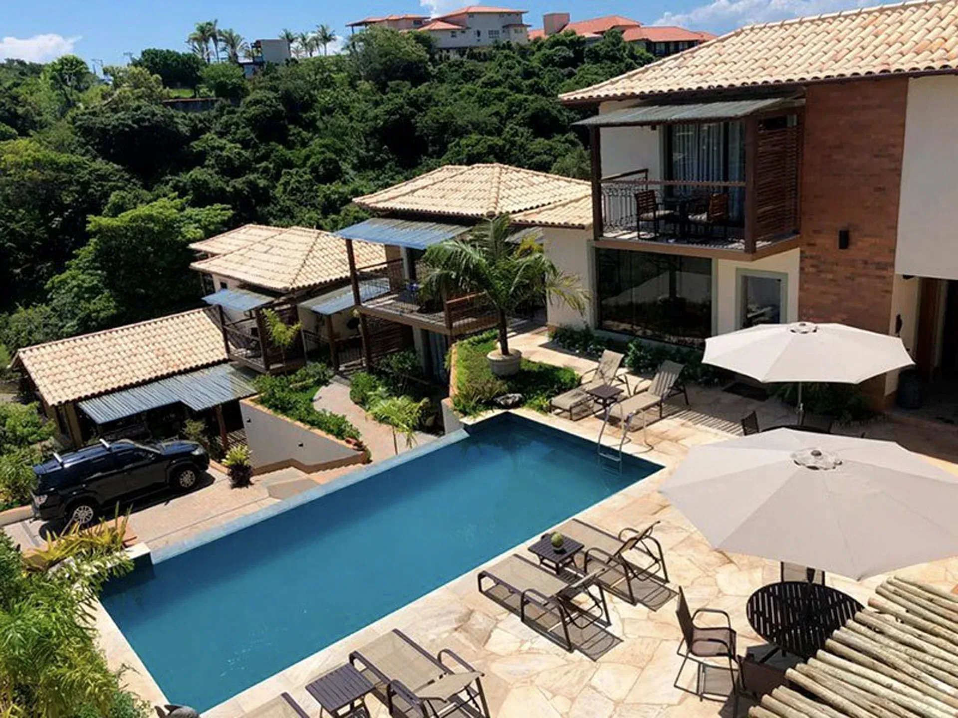 Villa de luxo com piscina azul, espreguiçadeiras e guarda-sóis no pátio com vista para uma vegetação exuberante.