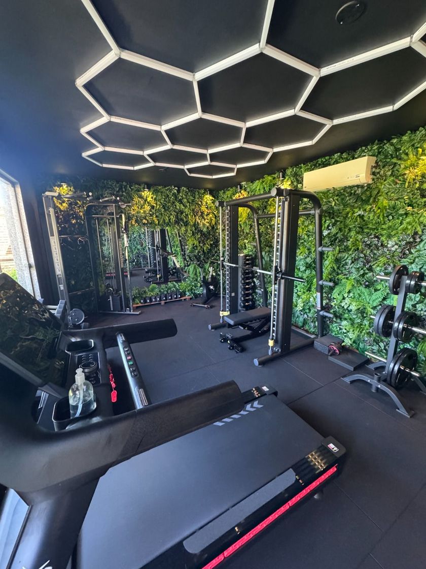 Academia moderna ao ar livre com esteiras, aparelhos de musculação e iluminação hexagonal de LED no teto.