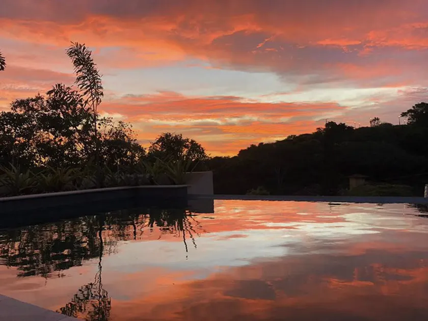 Céu ao pôr do sol refletido em um lago tranquilo ao lado de árvores e arbustos em silhueta.