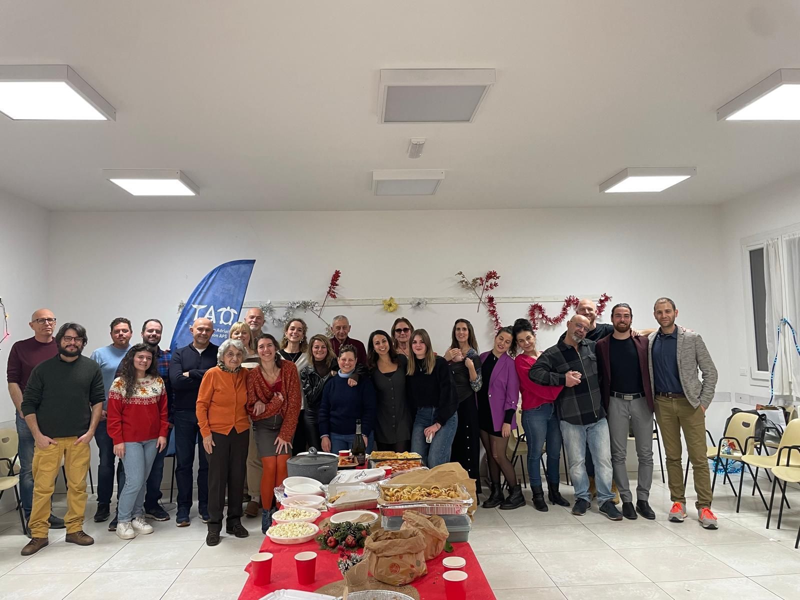 Un gruppo di persone è riunito in una stanza decorata, attorno a un tavolo imbandito con cibo e bevande.