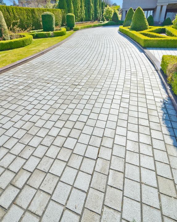 A brick driveway leading to a house surrounded by trees and bushes.