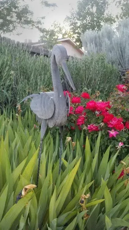 A statue of a bird is standing in a garden surrounded by flowers.
