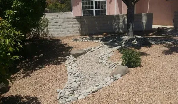 A rocky path leading to a house with a pink building in the background.