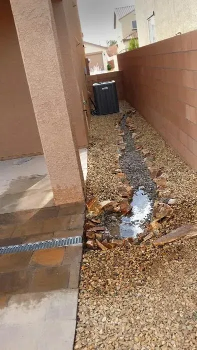 A drain in a backyard next to a brick wall with water coming out of it.