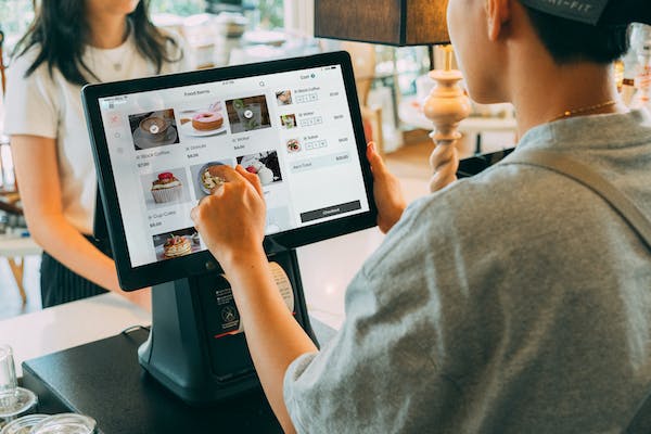 Person using a touchscreen POS system at a bakery counter, selecting items for a customer.