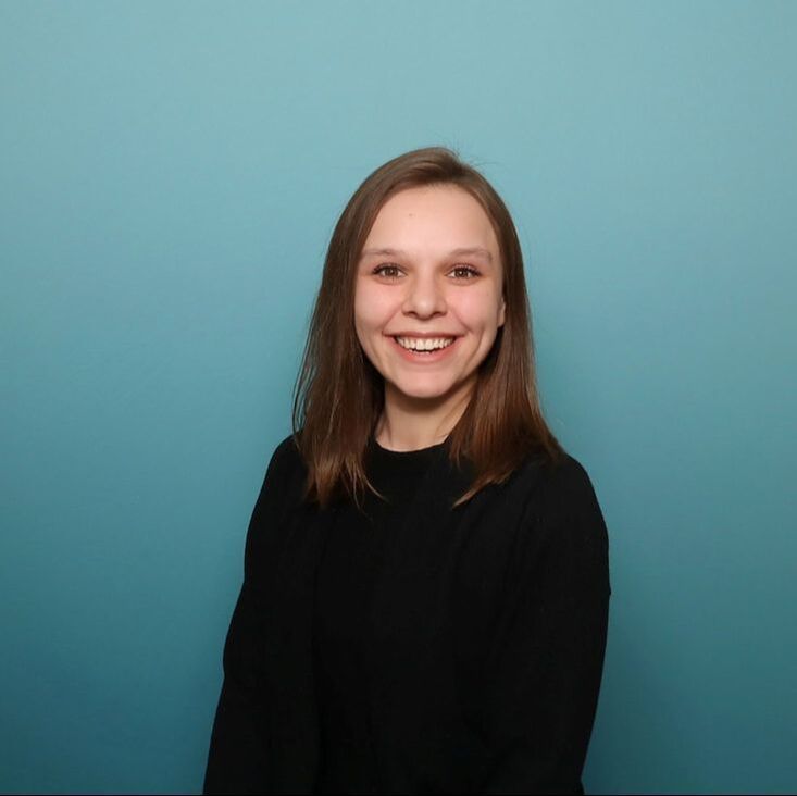Smiling person in a black top against a teal background
