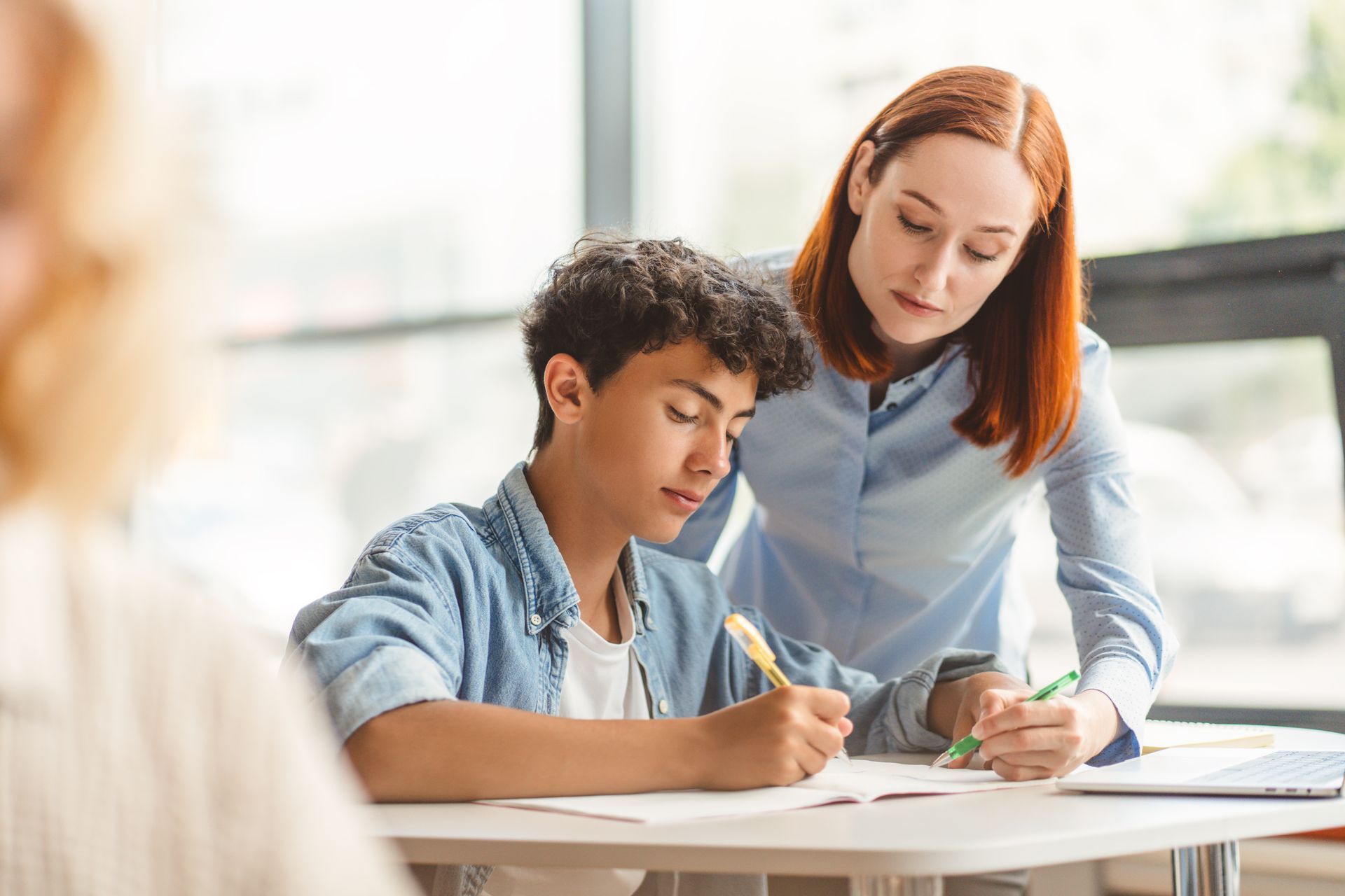 Teacher helping a student with a worksheet in a bright classroom