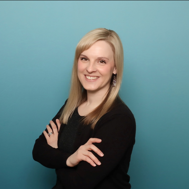 Smiling blonde person with crossed arms in a black top against a blue background