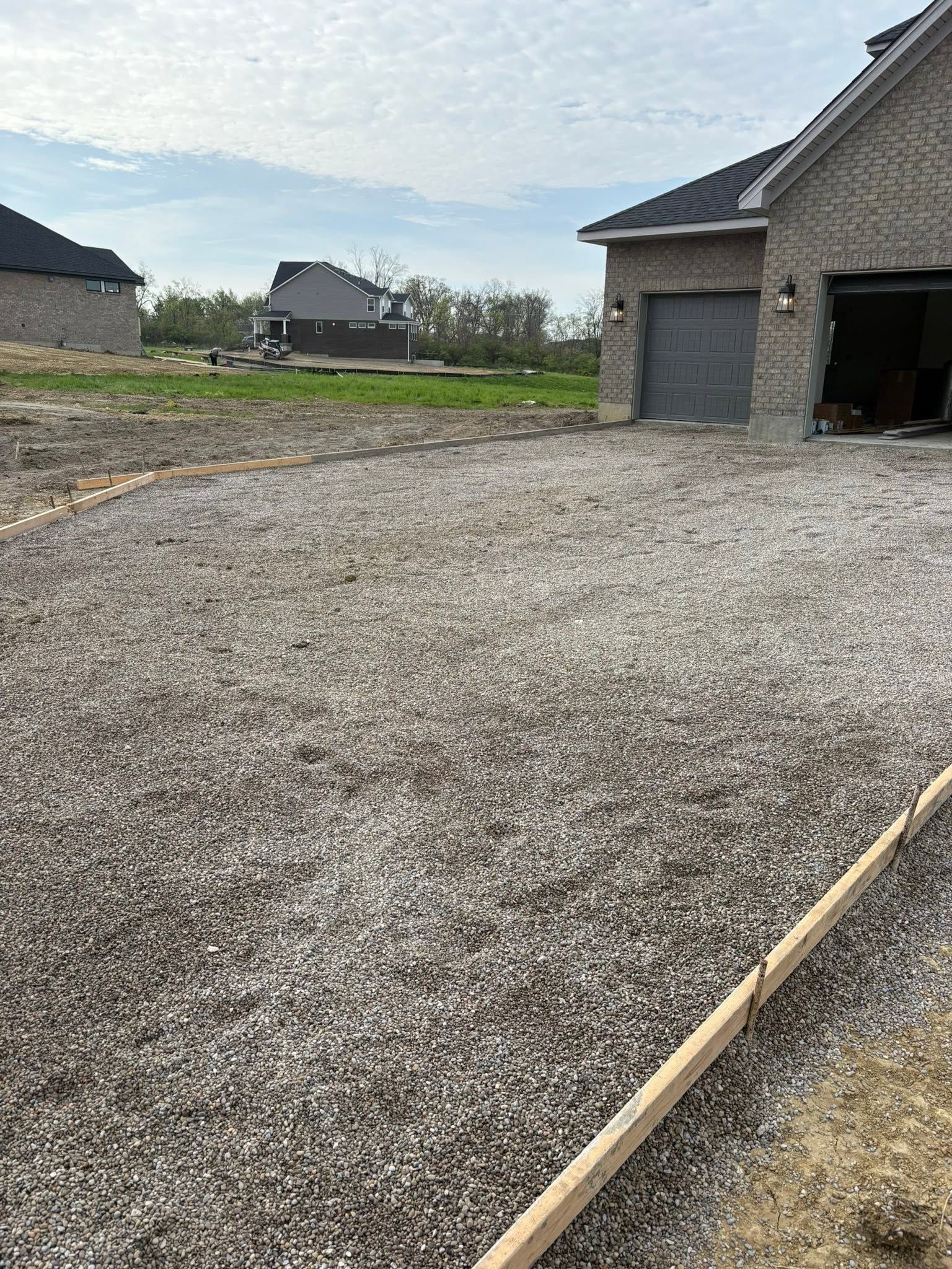 Gravel driveway leading to a garage under construction in a suburban lot, with houses in the background.
