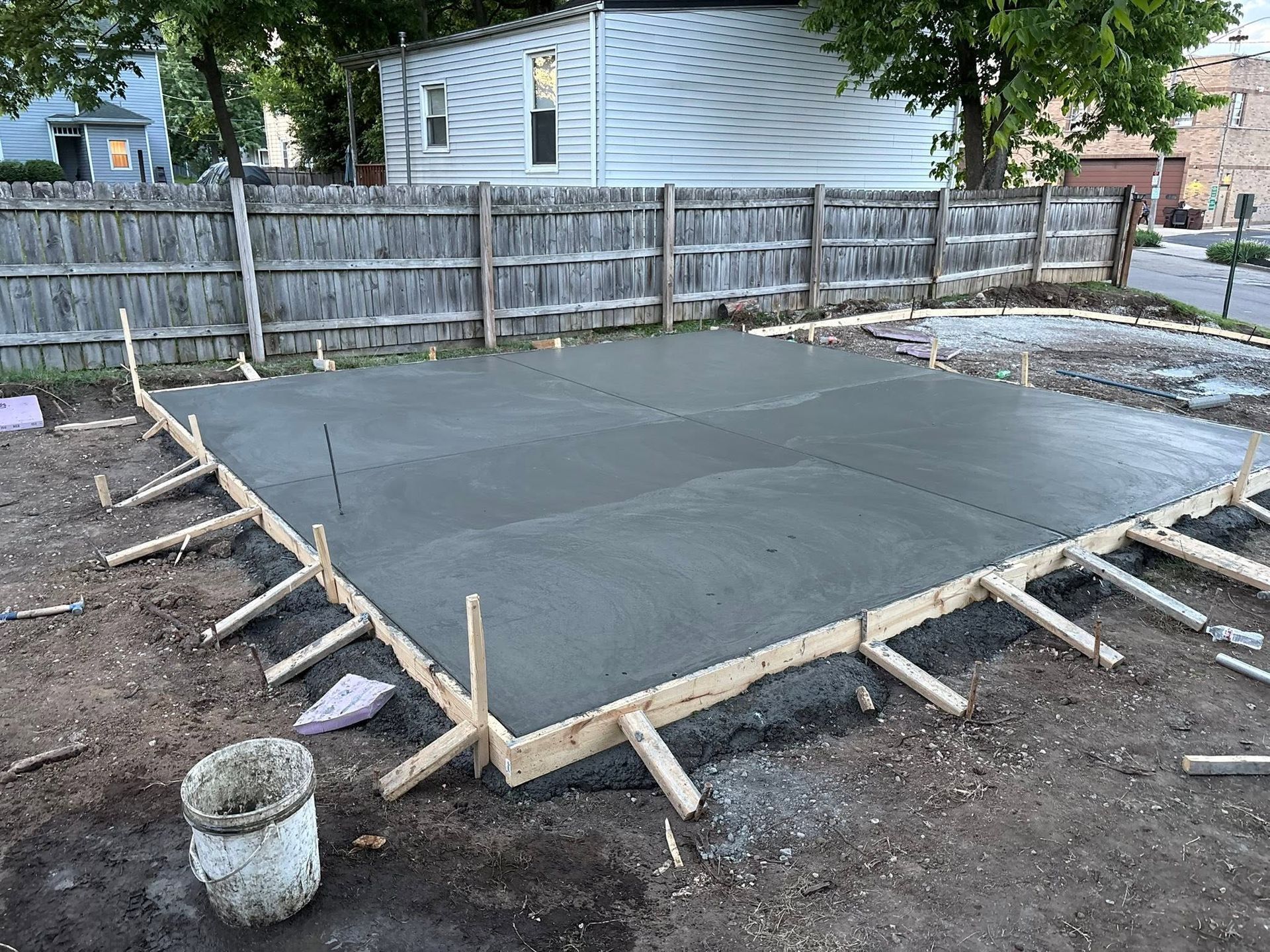 Freshly poured concrete slab with wooden formwork in a fenced backyard