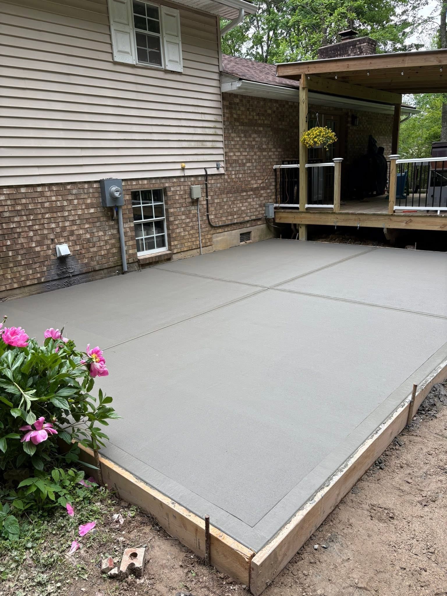 Fresh concrete patio beside house with porch and flowers