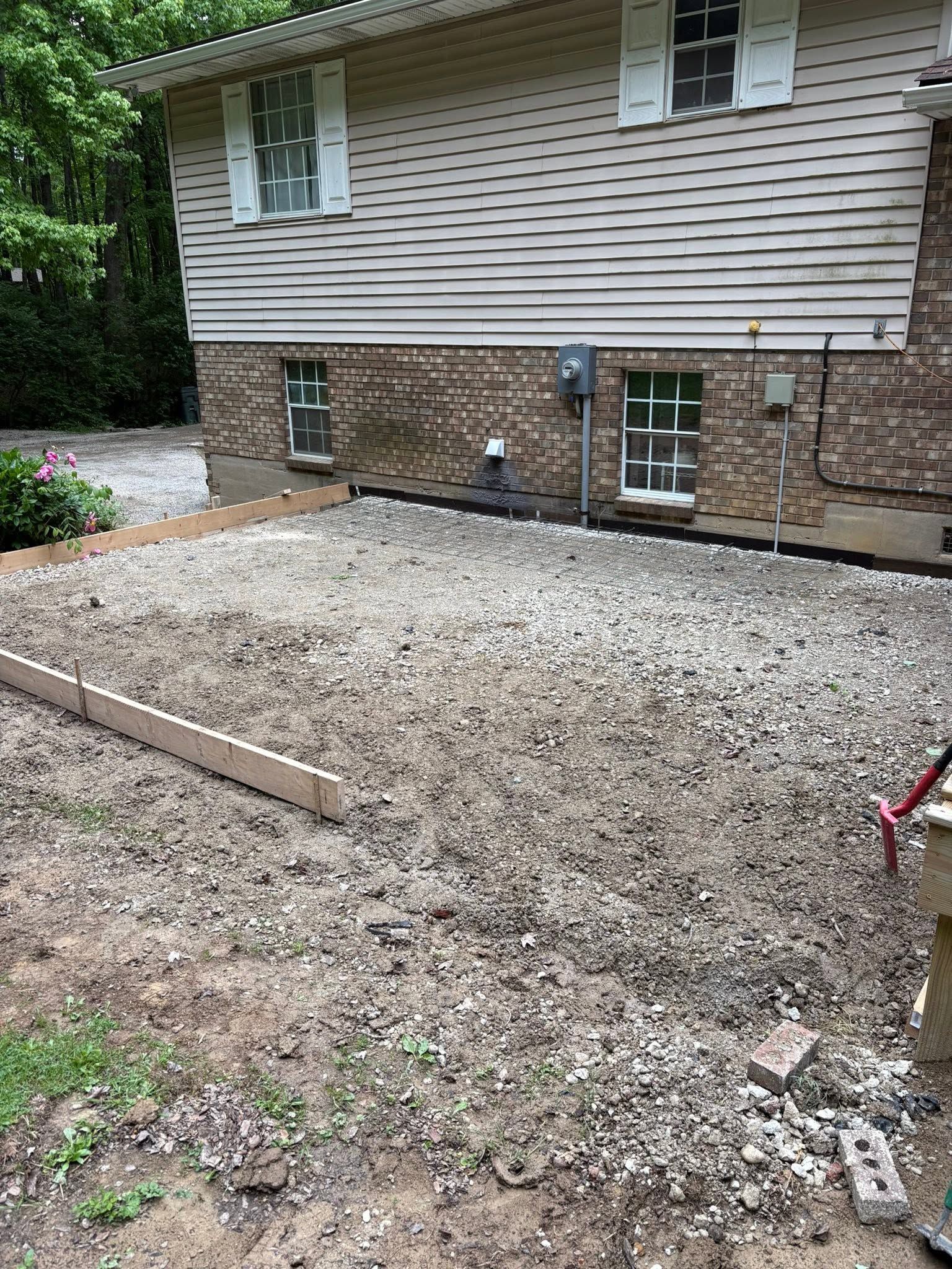 Gravel-covered backyard beside a house with beige siding and stone foundation, bordered by wooden edges and shrubs.