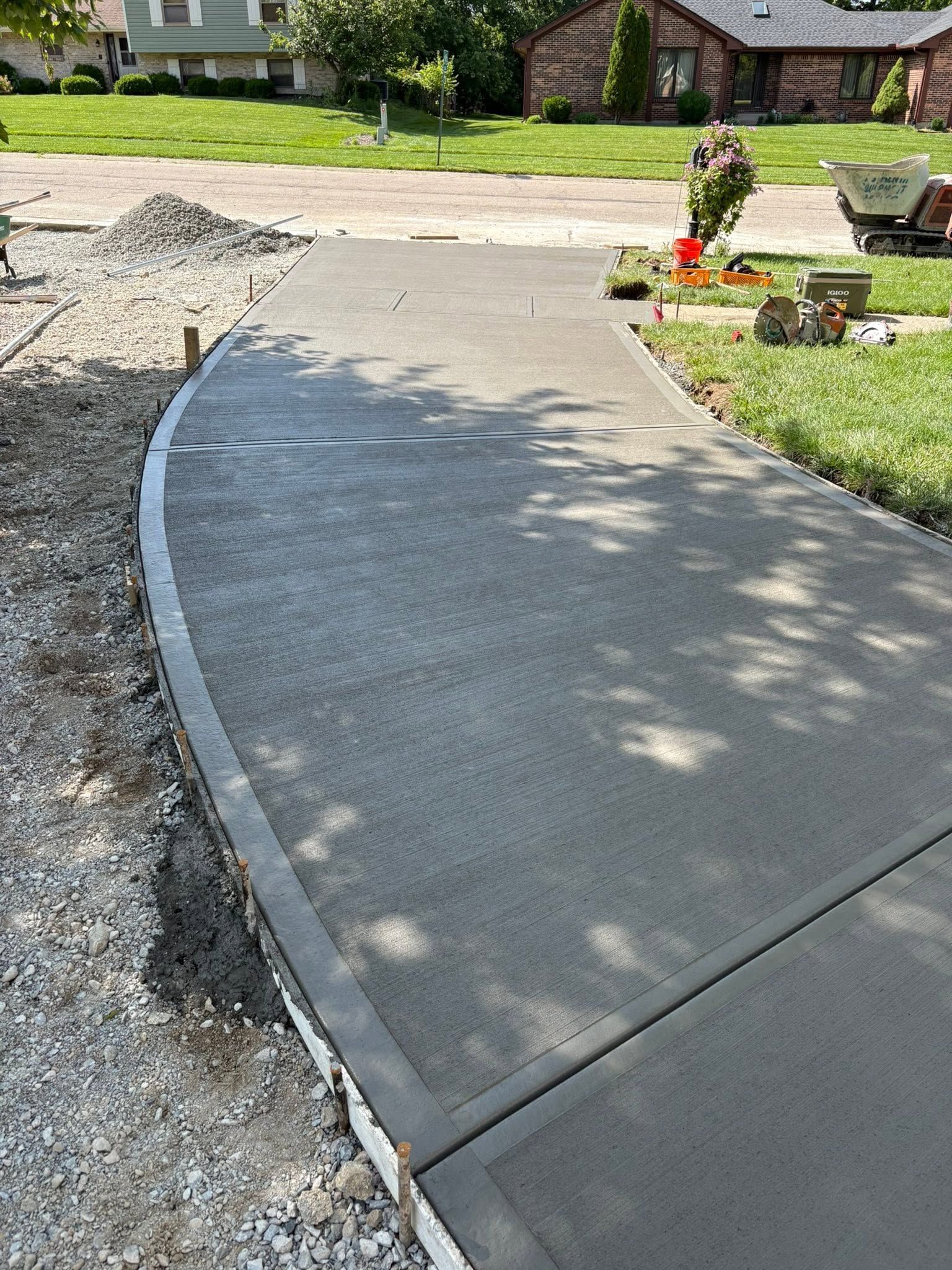 Curved concrete driveway edge beside gravel and a flower bed in a suburban yard