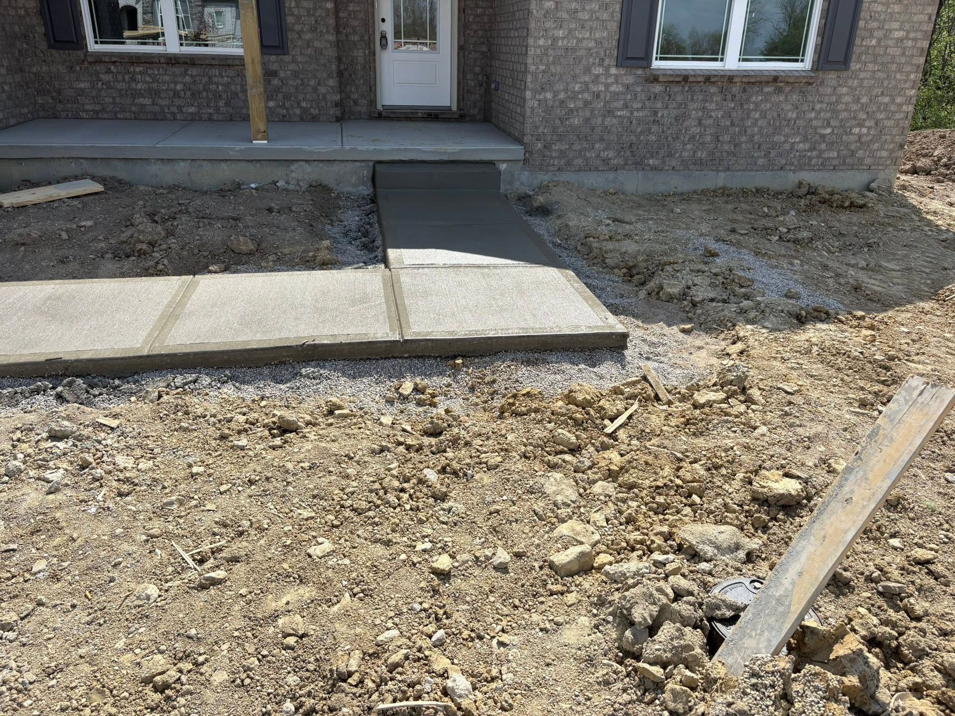 Front porch with concrete walkway and steps leading to a brick house, surrounded by bare dirt.