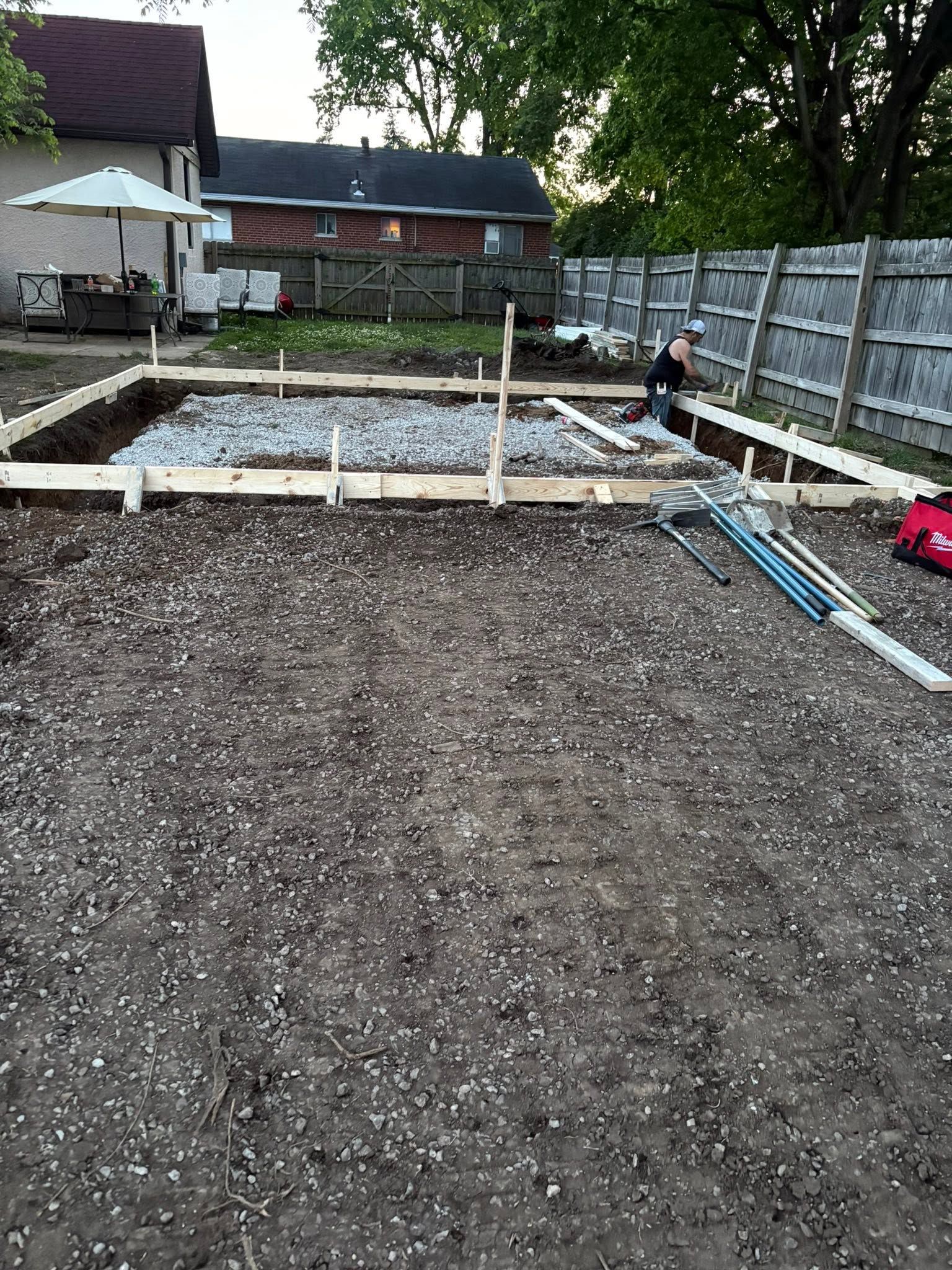 Garden area with gravel, wooden framing, and a person working near a fence and house.